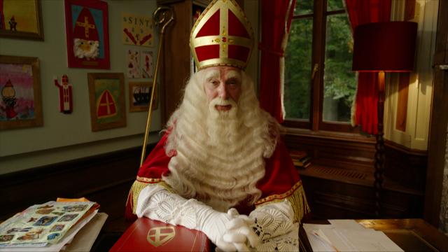 Sinterklaas zit achter zijn bureau en spreekt de camera toe.